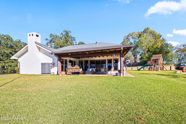 back of house featuring a lawn, an outdoor living space, a playground, central AC unit, and a patio area