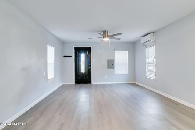 empty room with electric panel, an AC wall unit, ceiling fan, and light hardwood / wood-style floors