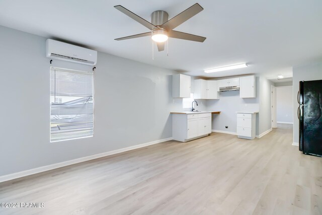 kitchen with a wall unit AC, black fridge, white cabinetry, and light wood-type flooring