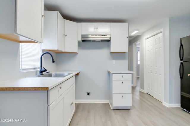 807 American Legion Dr, Rayne, LA 70578 - kitchen with under cabinet range hood, light wood-style floors, white cabinetry, light countertops, and freestanding refrigerator
