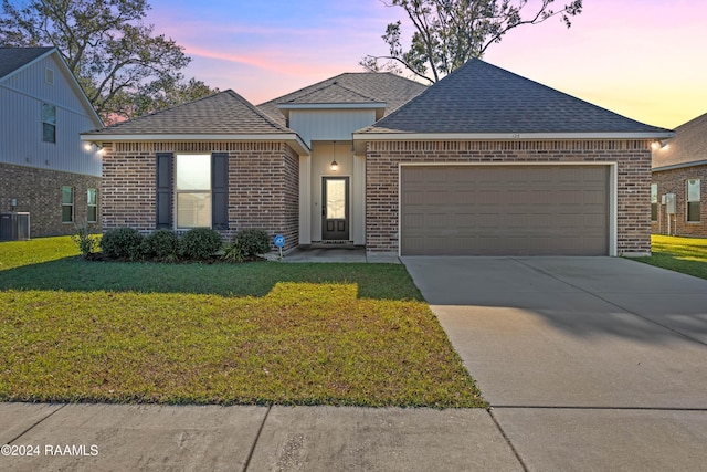 view of front of property with a garage, a yard, and central AC