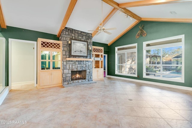 unfurnished living room with vaulted ceiling with beams, ceiling fan, a stone fireplace, and a wealth of natural light