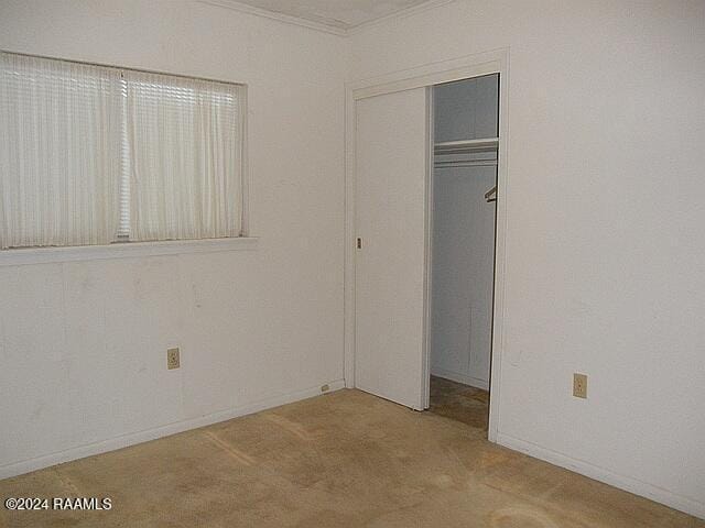 unfurnished bedroom featuring light colored carpet, crown molding, and a closet