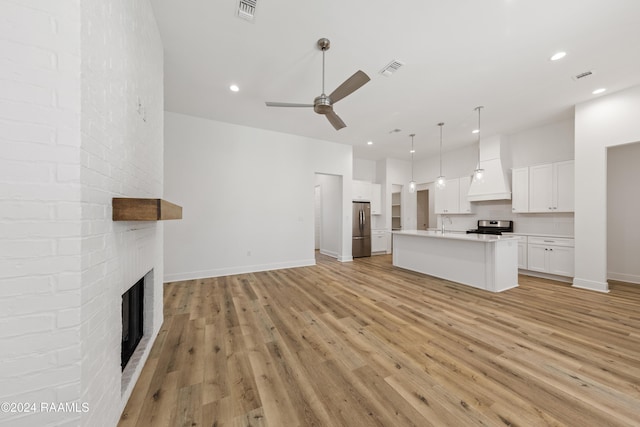 unfurnished living room with a brick fireplace, ceiling fan, sink, and light wood-type flooring