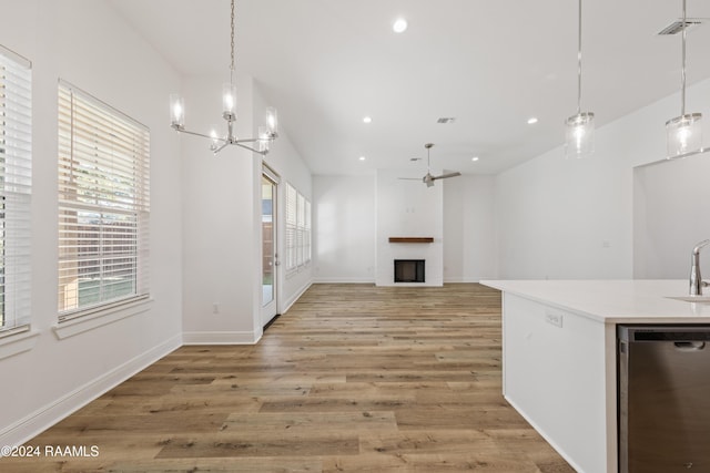 unfurnished living room with ceiling fan with notable chandelier, a large fireplace, sink, and light hardwood / wood-style flooring