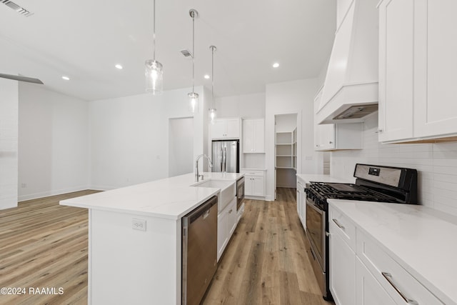 kitchen with white cabinetry, stainless steel appliances, light hardwood / wood-style flooring, premium range hood, and an island with sink