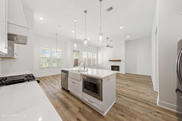 kitchen featuring sink, appliances with stainless steel finishes, pendant lighting, white cabinets, and light wood-type flooring