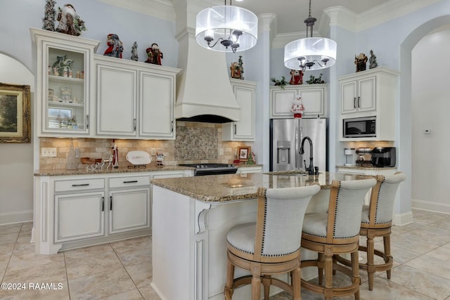 kitchen with sink, an island with sink, pendant lighting, custom range hood, and appliances with stainless steel finishes