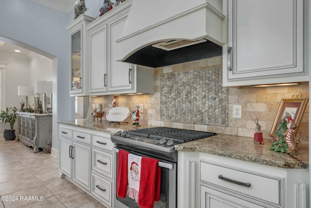 kitchen with decorative backsplash, ornamental molding, custom exhaust hood, gas range, and white cabinetry