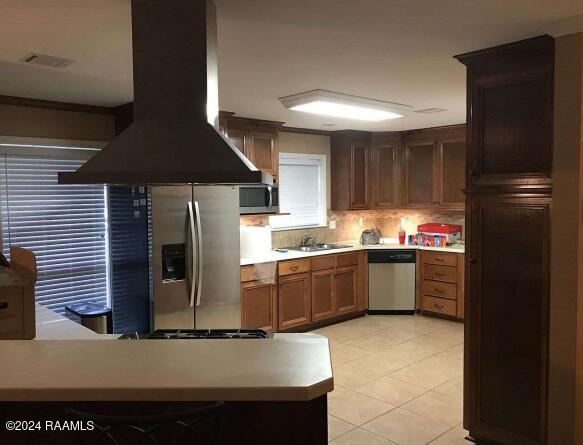 kitchen with sink, appliances with stainless steel finishes, tasteful backsplash, island range hood, and kitchen peninsula