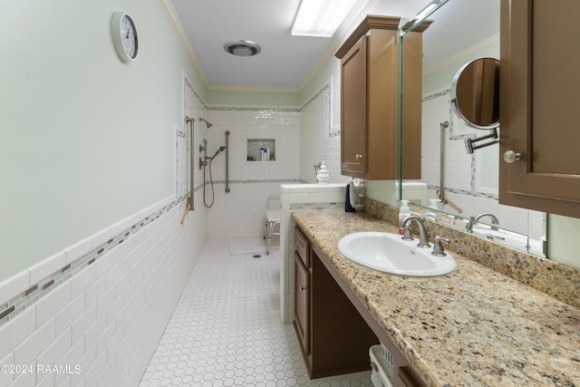 bathroom featuring vanity, a tile shower, ornamental molding, and tile walls