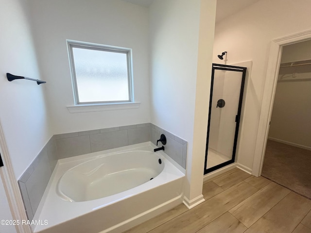 bathroom with a stall shower, a spacious closet, a bath, and wood finish floors