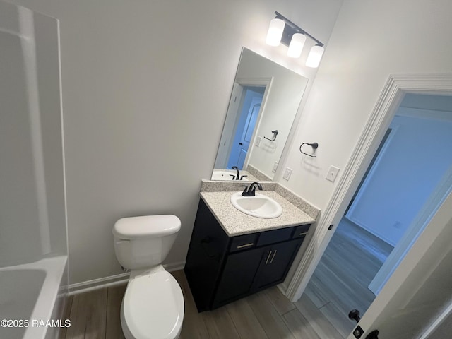 bathroom featuring toilet, baseboards, wood finish floors, and vanity