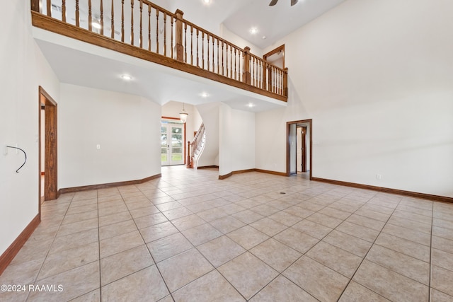 unfurnished living room featuring ceiling fan, a towering ceiling, and light tile patterned floors