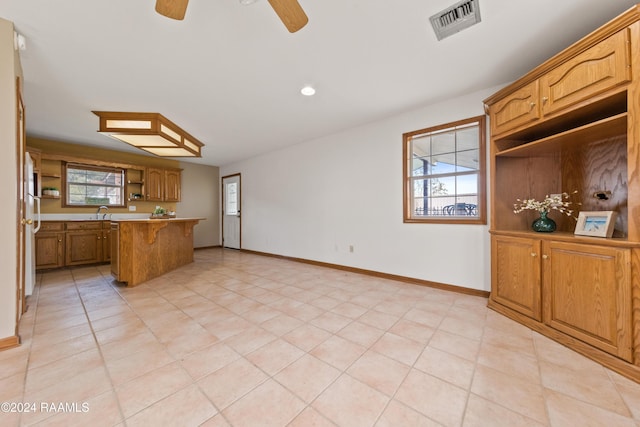 kitchen featuring a kitchen bar, ceiling fan, a healthy amount of sunlight, and light tile patterned flooring