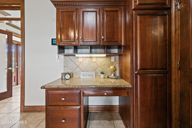 kitchen featuring light tile patterned floors, built in desk, light stone counters, and backsplash