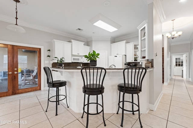 kitchen featuring light tile patterned floors, white appliances, a kitchen breakfast bar, white cabinets, and kitchen peninsula