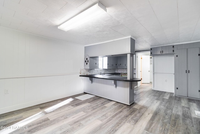 kitchen with kitchen peninsula, backsplash, gray cabinetry, hardwood / wood-style flooring, and a breakfast bar area