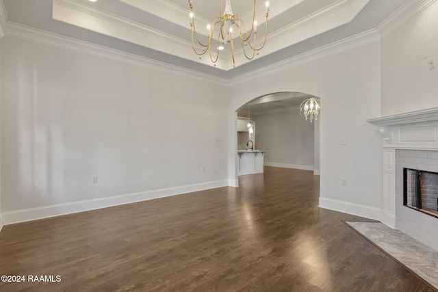 unfurnished living room featuring dark hardwood / wood-style flooring, a brick fireplace, ornamental molding, a raised ceiling, and a notable chandelier