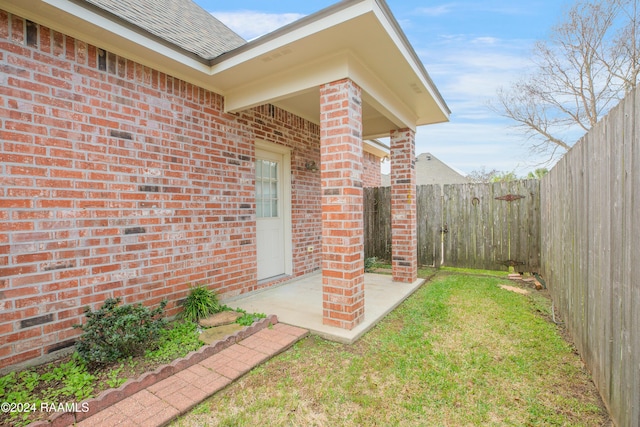 view of exterior entry featuring a patio and a lawn