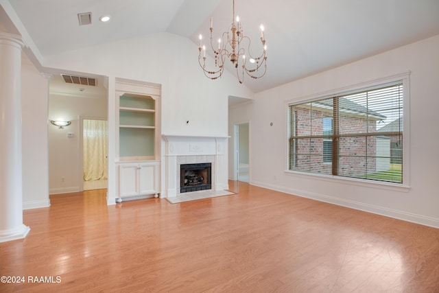 unfurnished living room with lofted ceiling, a tiled fireplace, light wood-type flooring, ornate columns, and a chandelier