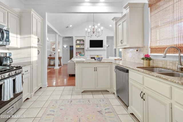 kitchen with appliances with stainless steel finishes, vaulted ceiling, sink, light tile patterned floors, and pendant lighting