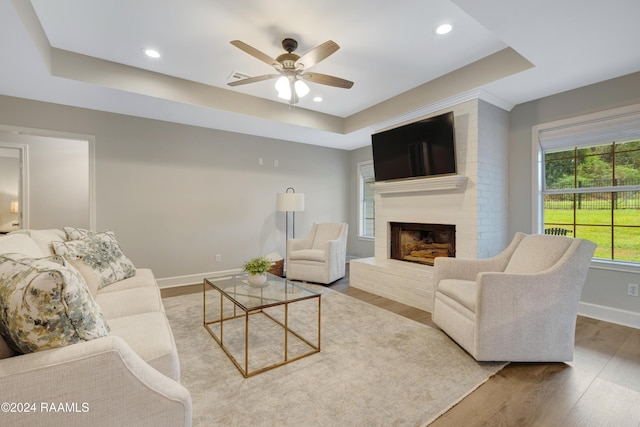 living room featuring a raised ceiling, ceiling fan, a fireplace, and hardwood / wood-style flooring