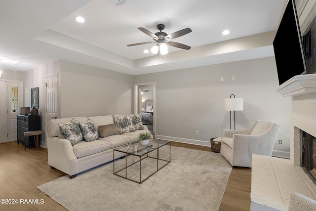 living room with a fireplace, light hardwood / wood-style floors, a raised ceiling, and ceiling fan