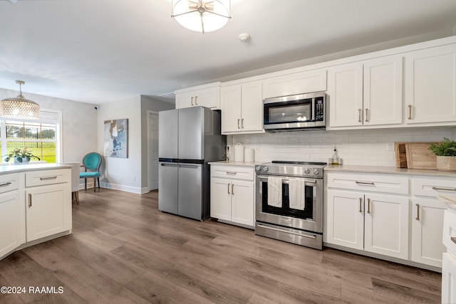 kitchen featuring white cabinets, hanging light fixtures, light hardwood / wood-style flooring, decorative backsplash, and appliances with stainless steel finishes