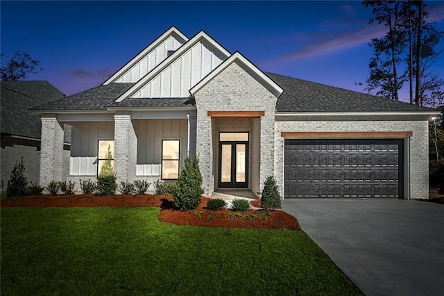 view of front of property with an attached garage, concrete driveway, roof with shingles, a lawn, and board and batten siding