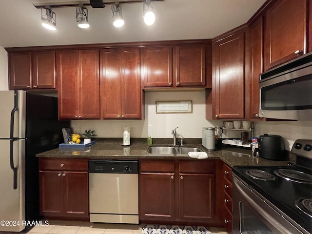 kitchen with dark stone countertops, sink, light tile patterned floors, and stainless steel appliances