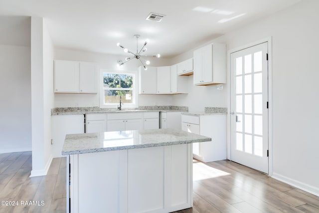 kitchen featuring light stone countertops, white cabinetry, sink, light hardwood / wood-style floors, and a kitchen island