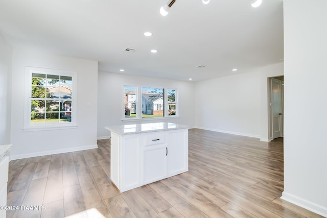 kitchen with light stone countertops, white cabinetry, a center island, and light hardwood / wood-style floors