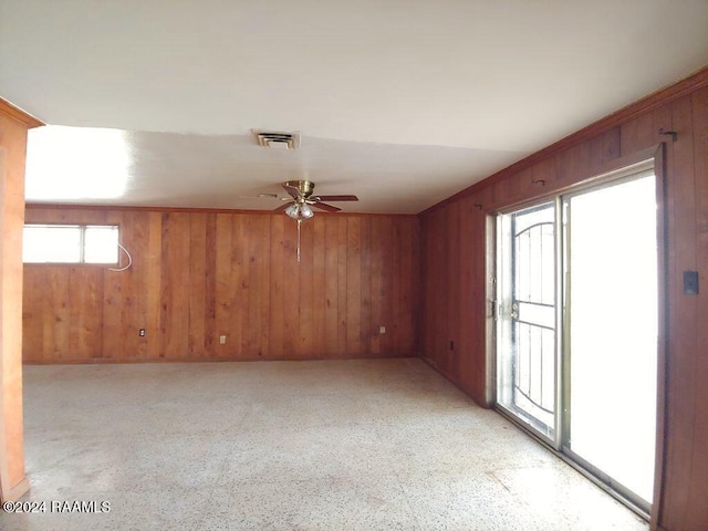 empty room featuring ceiling fan and wooden walls