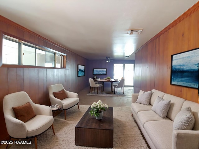 living room featuring ornamental molding, wood walls, and visible vents