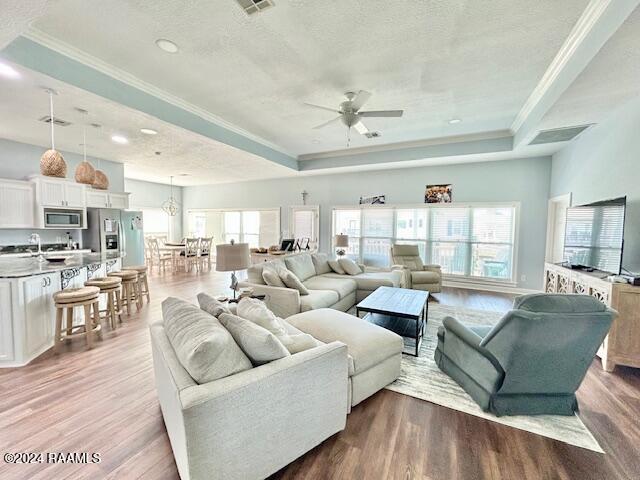 living room with light wood-type flooring, a tray ceiling, and ceiling fan