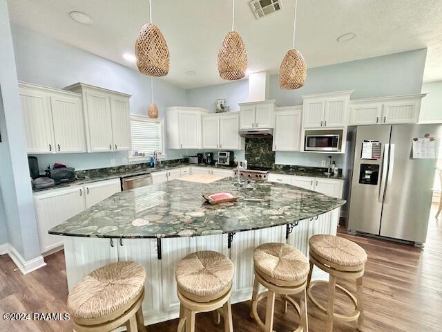 kitchen with hanging light fixtures, appliances with stainless steel finishes, dark hardwood / wood-style floors, and a kitchen island with sink