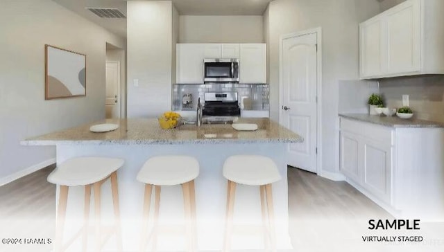 kitchen with appliances with stainless steel finishes, white cabinetry, a kitchen island with sink, and light stone counters