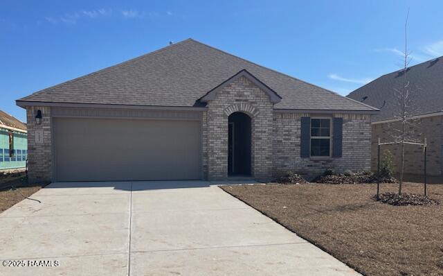 french provincial home with an attached garage, driveway, brick siding, and a shingled roof