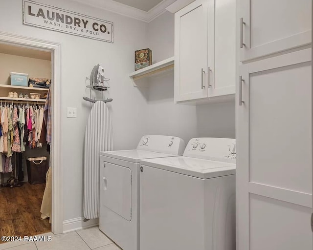 laundry area featuring washing machine and clothes dryer, crown molding, light tile patterned floors, and cabinets