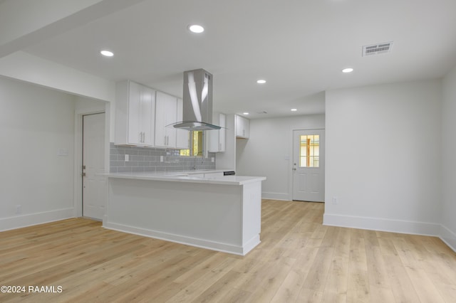 kitchen featuring white cabinetry, backsplash, island exhaust hood, kitchen peninsula, and light hardwood / wood-style floors