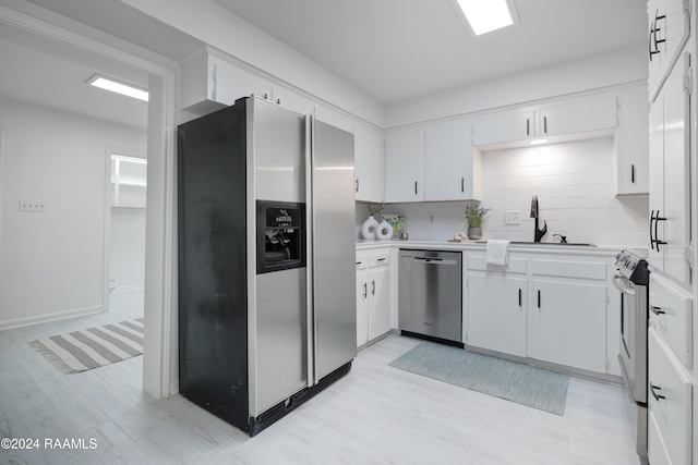 kitchen with backsplash, stainless steel appliances, white cabinetry, and light hardwood / wood-style floors