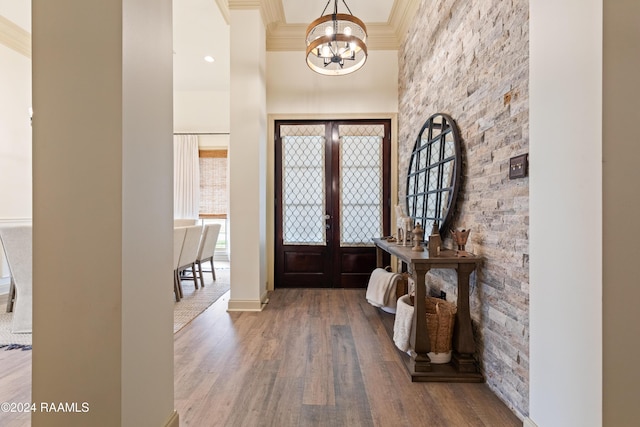 foyer entrance featuring french doors, crown molding, a towering ceiling, a chandelier, and wood-type flooring