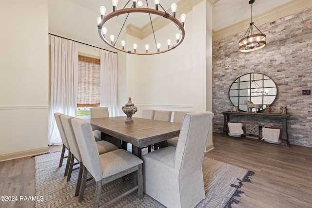 dining area with dark wood-type flooring, a towering ceiling, a chandelier, and ornamental molding