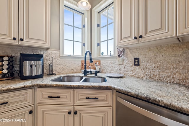 kitchen with stainless steel dishwasher, light stone counters, sink, and cream cabinets