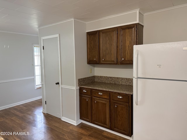 kitchen featuring dark stone countertops, dark hardwood / wood-style flooring, ornamental molding, and white refrigerator