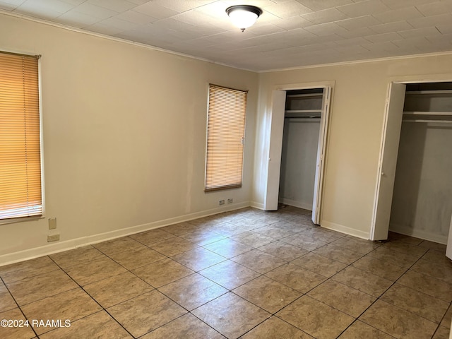 unfurnished bedroom featuring light tile patterned flooring, ornamental molding, and two closets