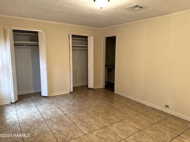 unfurnished bedroom featuring crown molding and multiple closets