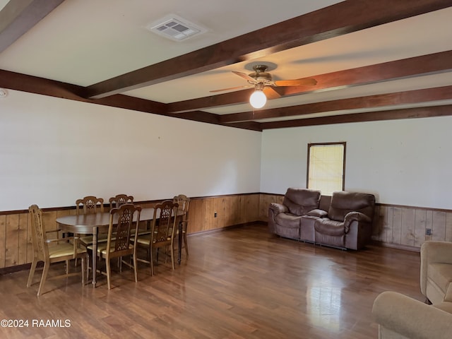 dining area featuring beam ceiling, dark hardwood / wood-style floors, ceiling fan, and wooden walls