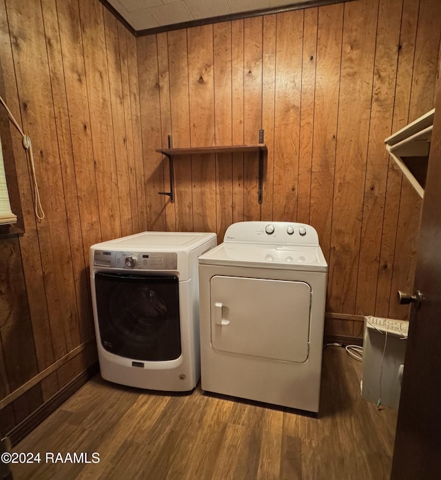 washroom with wood-type flooring, washer and clothes dryer, and wooden walls